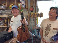 08 - Woodley White displays a newly built koa ukulele with a hand painted headstock, under the admiring eye of Rodney Crusat